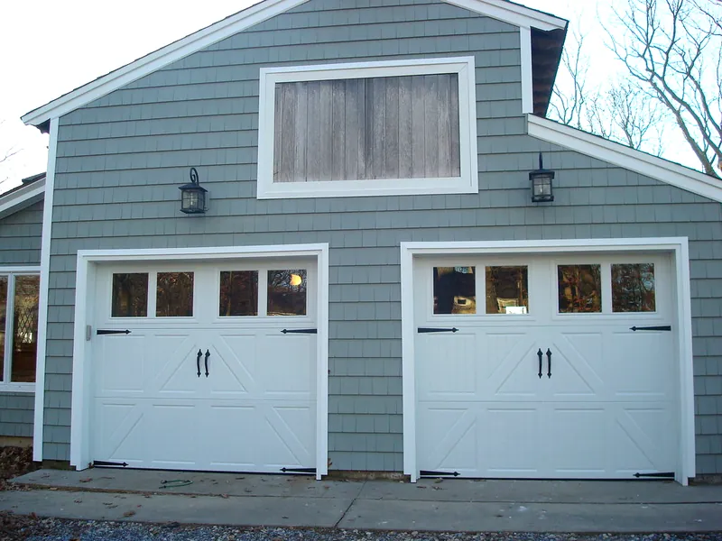Two white carriage-style garage doors with windows on a gray shingle garage